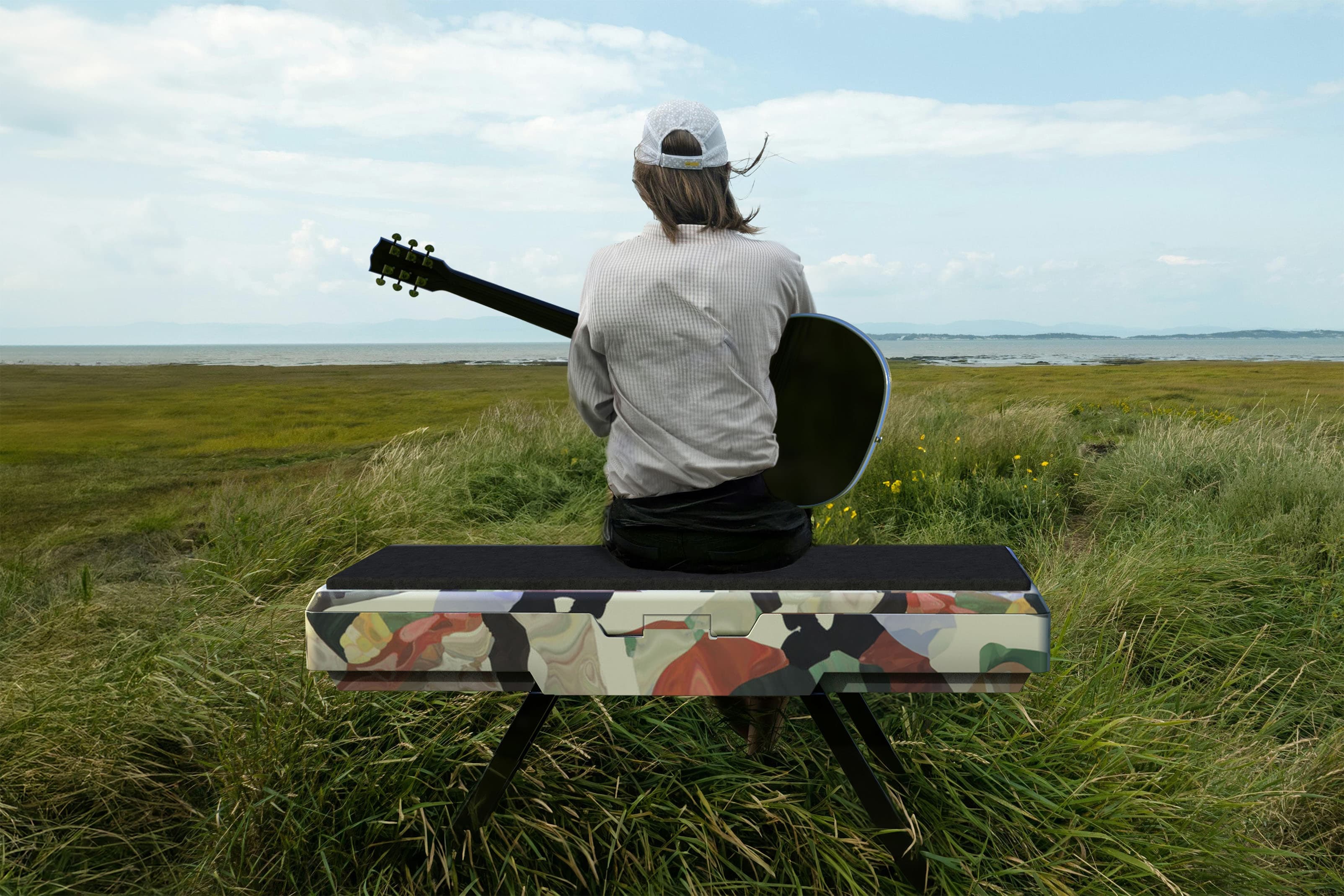 Behind view of a girl holding a guitar sitting on Rest, in a bench form, in the middle of a field.